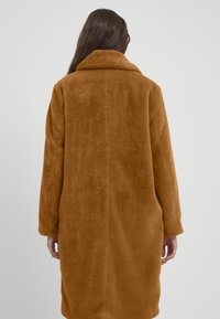 Brun faux fur frakke med høj krave, lange ærmer og lige silhuet, der har en blød tekstur og ingen synlige lukninger.