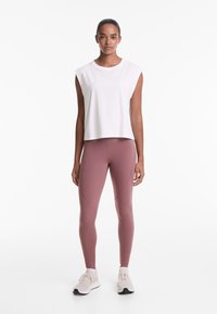 White sleeveless top with round neckline, paired with high-waisted, dusty rose leggings featuring panel accents and soft texture. Neutral sneakers.