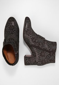 Botas de tobillo marrones y negras con un patrón texturizado, que cuentan con una cremallera lateral y un tacón bajo. Se puede ver el forro interior liso.