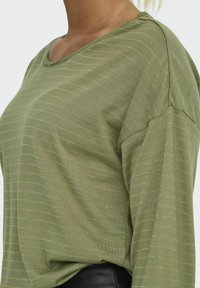 Olijfgroene langslavige top met horizontale gouden strepen, ronde halslijn en een ontspannen pasvorm. Zachte textuur met verlaagde schoudernaden.