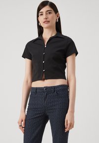 Zwart cropped shirt met korte mouwen, knoopsluiting aan de voorkant en een puntige kraag, gecombineerd met donkergepatroneerde jeans met een subtiele geometrische print.