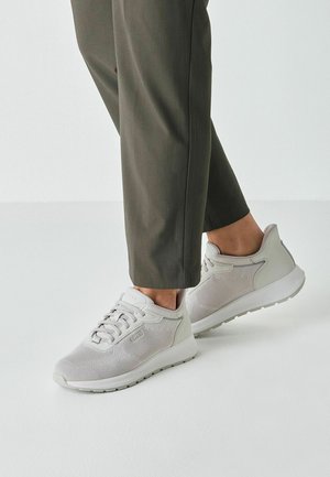 Hellgraue Sneakers mit mesh-Obermaterial, strukturierten Akzenten und Gummisohle. Kombiniert mit olivgrünen, maßgeschneiderten Hosen.