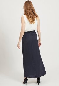 Lång marinblå kjol med elastisk midja och en mjuk textur, kombinerad med en figurnära vit ärmlös topp. Enkelt design, utan mönster.