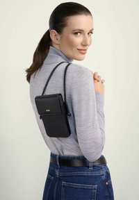 Czarna pikowana torebka crossbody z klapą i regulowanym paskiem, noszona na plecach. Ustawiona na jasnym tle, w połączeniu z szarym topem.