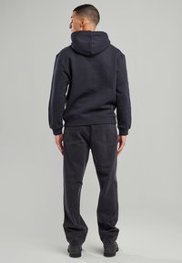 Tummansininen fleece-huppari, jossa on naru-huppu ja ribbireunat, yhdistettynä tummanharmaisiin rentoihin farkkuihin, joissa on kaksi takataskua.