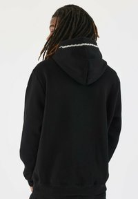 Sudadera negra con capucha ajustable, con un acento texturizado blanco a lo largo del escote, hecha de un tejido suave y con un corte relajado.