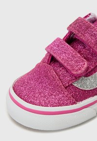 Baskets à paillettes roses avec des brides Velcro et un logo en accent argenté ; elles disposent d'une semelle en caoutchouc blanche et d'un dessus en paillettes texturé.
