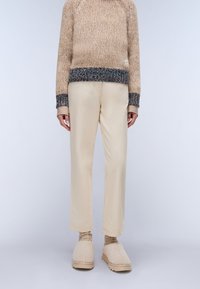 Beige knitted sweater with textured yarn, cream tailored pants, and light beige slippers. Sweater features a multicolored ribbed hem.