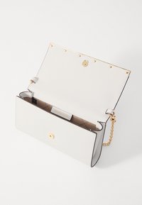 Sac à main blanc avec une finition texturée, quincaillerie dorée, fermeture magnétique et une bandoulière en chaîne amovible. L'intérieur présente un logo et un compartiment.