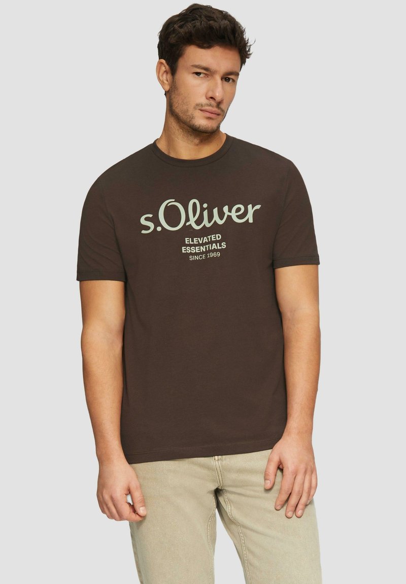 Ruskea puuvillat-paita, jossa on kerma "s.Oliver" -logo ja tekstimuotoilu. Lyhyet hihat ja pyöreä pääntie.