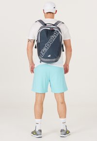Mochila gris y negra con el logo "Babolat", correas ajustables, bolsillos laterales y un bolsillo frontal con cremallera, con una tela suave y duradera.