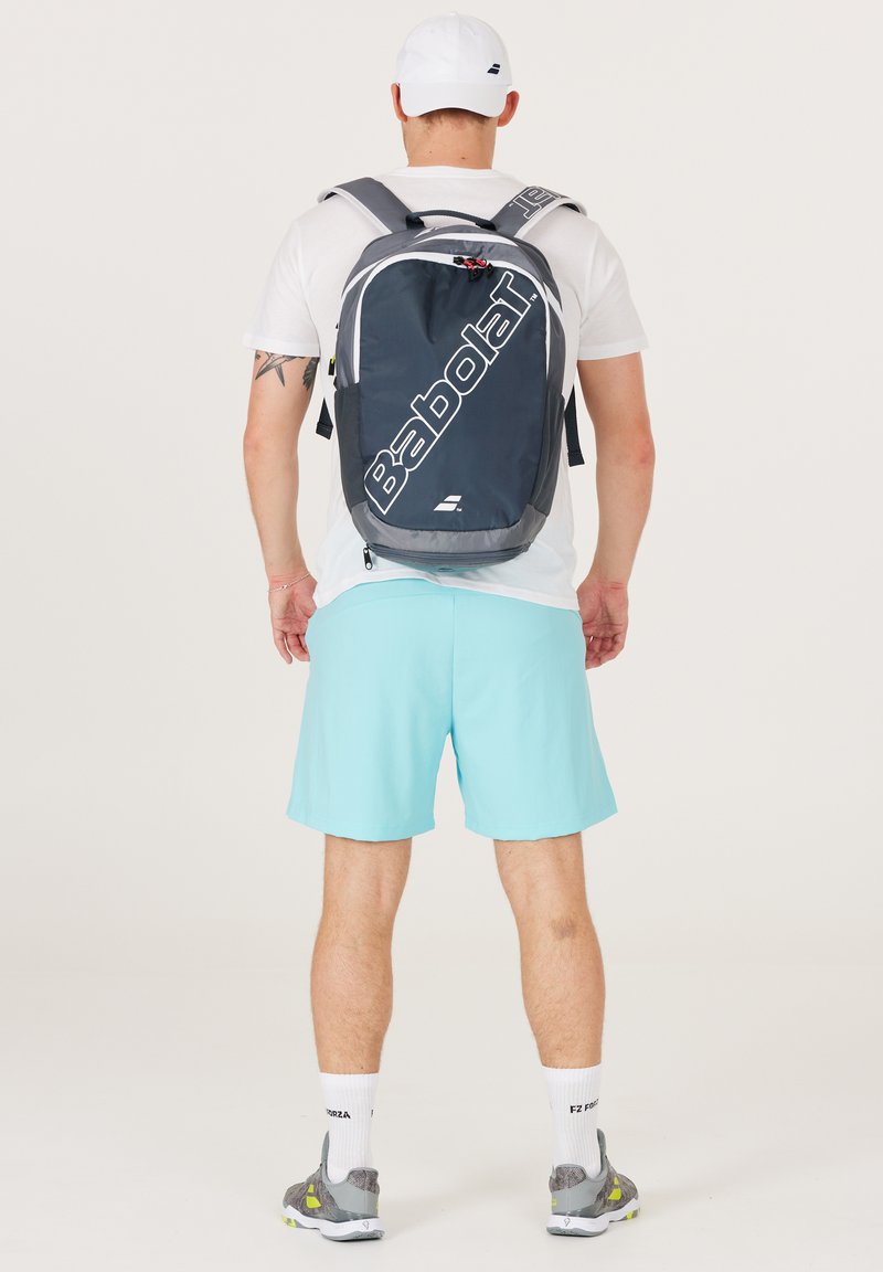 Mochila gris y negra con el logo "Babolat", correas ajustables, bolsillos laterales y un bolsillo frontal con cremallera, con una tela suave y duradera.