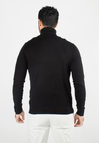 Pull en col roulé noir ajusté, avec des manches longues et un col côtelé. Le tissu semble lisse avec un minimum de détails.
