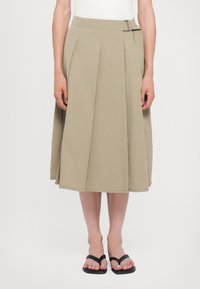 O fustă midi khaki cu un design plisat, talie plată și detaliu cu cataramă pe lateral. Fabricată dintr-un material ușor.
