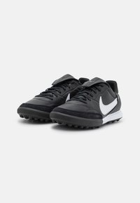 Zapatillas deportivas negras que presentan un material de cuero sintético, un diseño con cordones, el logotipo en blanco de Swoosh y una suela de goma texturizada con tachuelas.