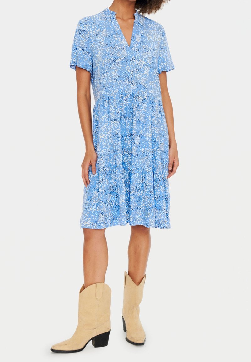 Robe florale bleue avec un col en V, des manches courtes et une taille froncée. Une paire de bottes de cow-boy beiges avec un talon carré.