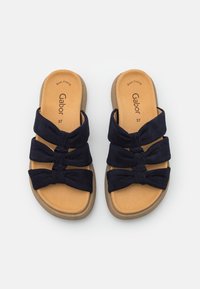 Marinblåa slidesandaler i mjukt mockamaterial med tre knutna band och en beige vadderad sula. Varumärkeslogotyp synlig på inläggssulan.