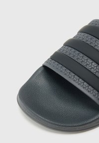 Tmavošedá šľapka na podrážke s textúrovaným remienkom s tromi hladkými akcentmi, mäkkou stielkou a zaoblenou špičkou.