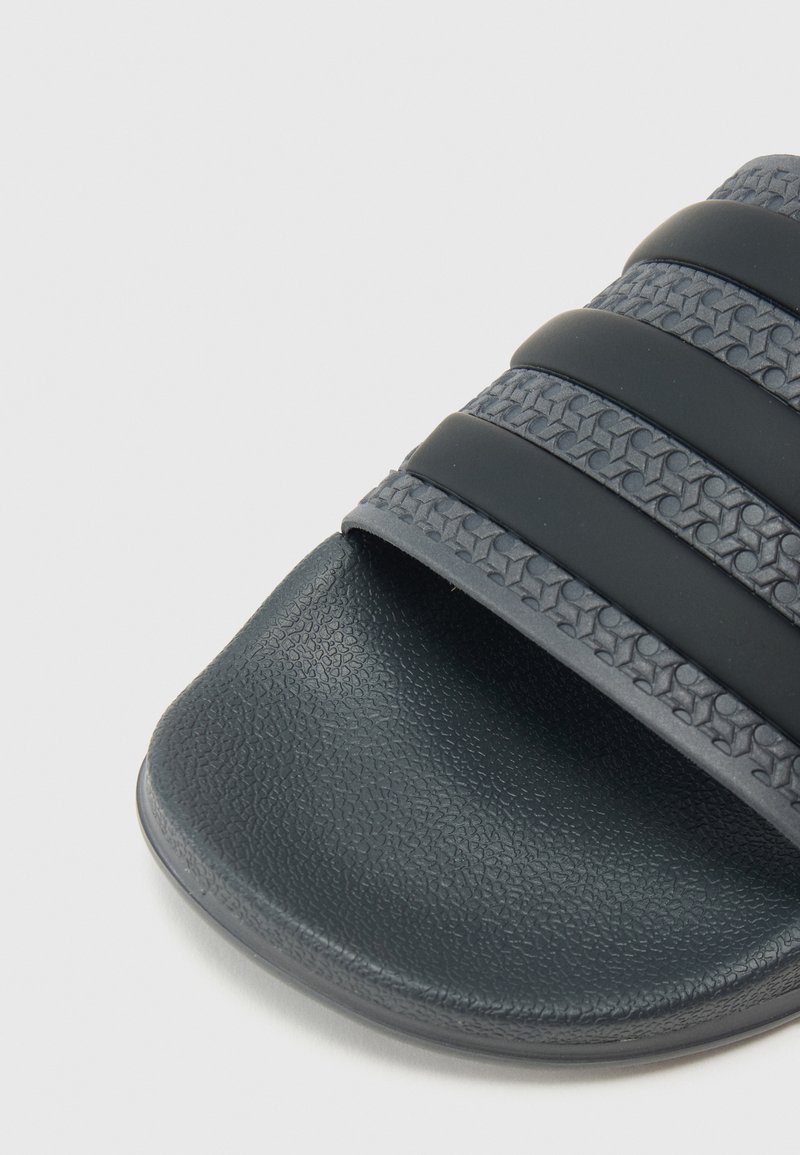 Sandale à glissière gris foncé avec une bride texturée ornée de trois bandes lisses, une semelle intérieure douce et un bout arrondi.