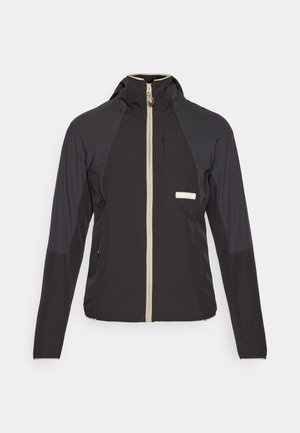 Svart zip-up jakke med hette, med en beige glidelås, kontrasterende skulderpaneler og en brystlomme. Laget av lett stoff.