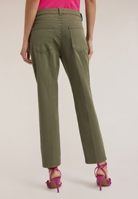 Oliwkowe spodnie o szerokich nogawkach z gładką teksturą, z dwoma tylnymi kieszeniami i wysokim stanem. W zestawie z różowymi sandałami na obcasie.