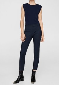 Marineblauwe geribbelde mouwloze top gecombineerd met strakke marineblauwe broek. Het model draagt zwarte enkellaarsjes met een metallic teen detail.