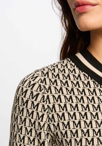 Knit sweater featuring a beige and black pattern with repeating letters. Black ribbed collar accents the design. Smooth texture, casual fit.