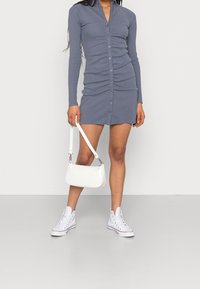 Långärmad, knappad klänning i skräddarsydd blå tyg med rynkdetaljer. Matchad med vita sneakers och en liten vit handväska.