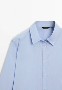 Light blue striped button-up shirt with a collared neck, featuring white buttons and a smooth fabric texture.