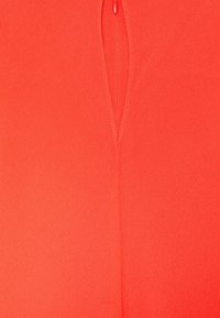 Lys orange tyg med en central söm och en liten, glansig orange pärla sydd längst upp på sömmen.