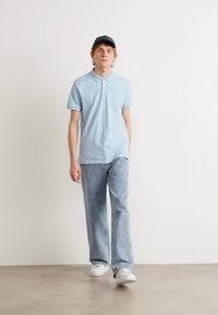 Svetlo modra polo majica, modri kavbojke, bele teniske in temna kapa; sproščen outfit z mehkimi materiali in udobnim krojem.