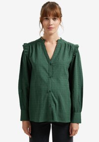 Green button-up shirt with a textured pattern, ruffled shoulders, and long sleeves. Features a V-neckline and relaxed fit.