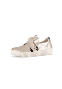 Jasno beżowy sneakers z metalicznym wykończeniem, elastycznymi paskami i teksturowaną białą podeszwą. Posiada czarne akcenty i niski profil.