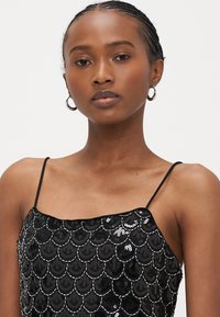 Fekete flitteres ruha hullámos mintával, spagettipántokkal és sima textúrával. Csillogó gyöngyszerű díszítésekkel kiemelve.