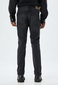 Jeans de mezclilla negra con un corte ajustado, que cuentan con dos bolsillos traseros y un parche de cuero en la cinturilla. Textura suave con un ligero desvanecimiento.