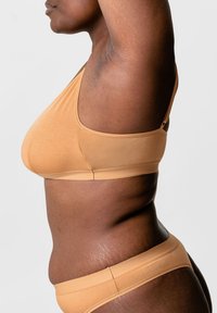 Zachte, tan-kleurige bralette met een naadloos ontwerp en zonder beugel. De stof heeft een gladde, rekbare textuur, wat comfort en ondersteuning biedt.