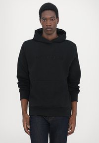 Black cotton hoodie featuring a front pocket and embossed "QUARTZ CO" logo. Soft texture, relaxed fit, and ribbed cuffs and hem.
