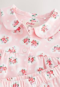 Lyserødt børne-pyjamasæt med hvidt hjerte- og pink blomsterprint samt rund krave.