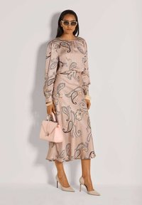 Helles rosa Satin-Kleid mit Paisleymuster, langen Ärmeln und taillierter Passform. Kombiniert mit einer pinken Handtasche und beigen High Heels.
