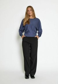 Maglione leggero blu con maniche lunghe, scollo rotondo e orlo a coste, abbinato a pantaloni a zampa neri a vita alta e scarpe nere.