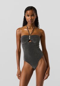 Mustast sädelevast materjalist üheosaline ujumistrikoo, millel on bandeau-stiilis ülaosa, avause detail ja õhukesed, reguleeritavad sangad. Kõrged lõigud jalgade ümber ja sileda tekstuuriga.