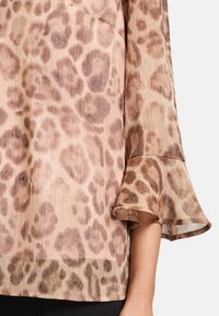 Blusa con stampa leopardata in tonalità beige e marrone, caratterizzata da maniche a campana e una texture plissettata con sottili accenti metallici.
