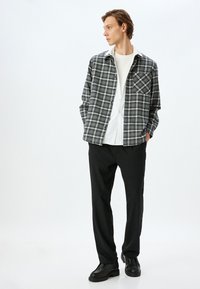 Sort-hvidt ternet skjorte med knappelukning og brystlomme, lagdelt over en hvid skjorte, parret med sorte bukser og sorte støvler.