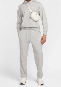 Grå bomullshoodie med dragsko och vitt logotyp, i kombination med matchande sweatpants. Accent: liten branding, kompletterad med en lätt krämfärgad crossbody-väska.