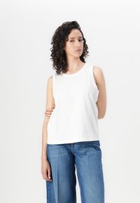 Top branco sem mangas com decote redondo, feito de um tecido suave. Combinado com jeans de perna larga azul claro, apresentando um corte casual.