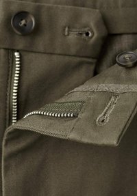 Pantaloni kaki con chiusura a zip e bottone, caratterizzati da un tessuto strutturato e dettagli di cuciture visibili, inclusa un'apertura per tasca.