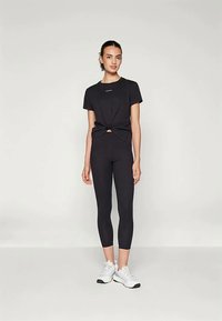 Crna atletska odjeća koja se sastoji od čvoraste majice i skraćenih tajica, oboje od glatke tkanine, uparena s bijelim sportskim tenisicama.