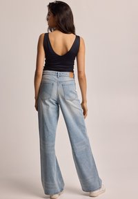 Top negro sin mangas con espalda baja, combinado con unos vaqueros de pierna ancha de color azul claro que tienen bolsillos traseros y una etiqueta de cuero marrón.