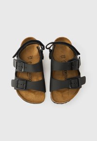 Crne kožne sandale s dvije podesive trake i kopčama, oblikovanom smeđom pluto tabanicom, ravnim potplatom, minimalističkim dizajnom i bez vidljivih uzoraka.