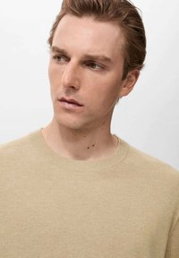 Beige knitted sweater with a ribbed crew neckline and a textured finish. The fabric appears soft with a subtle pattern.